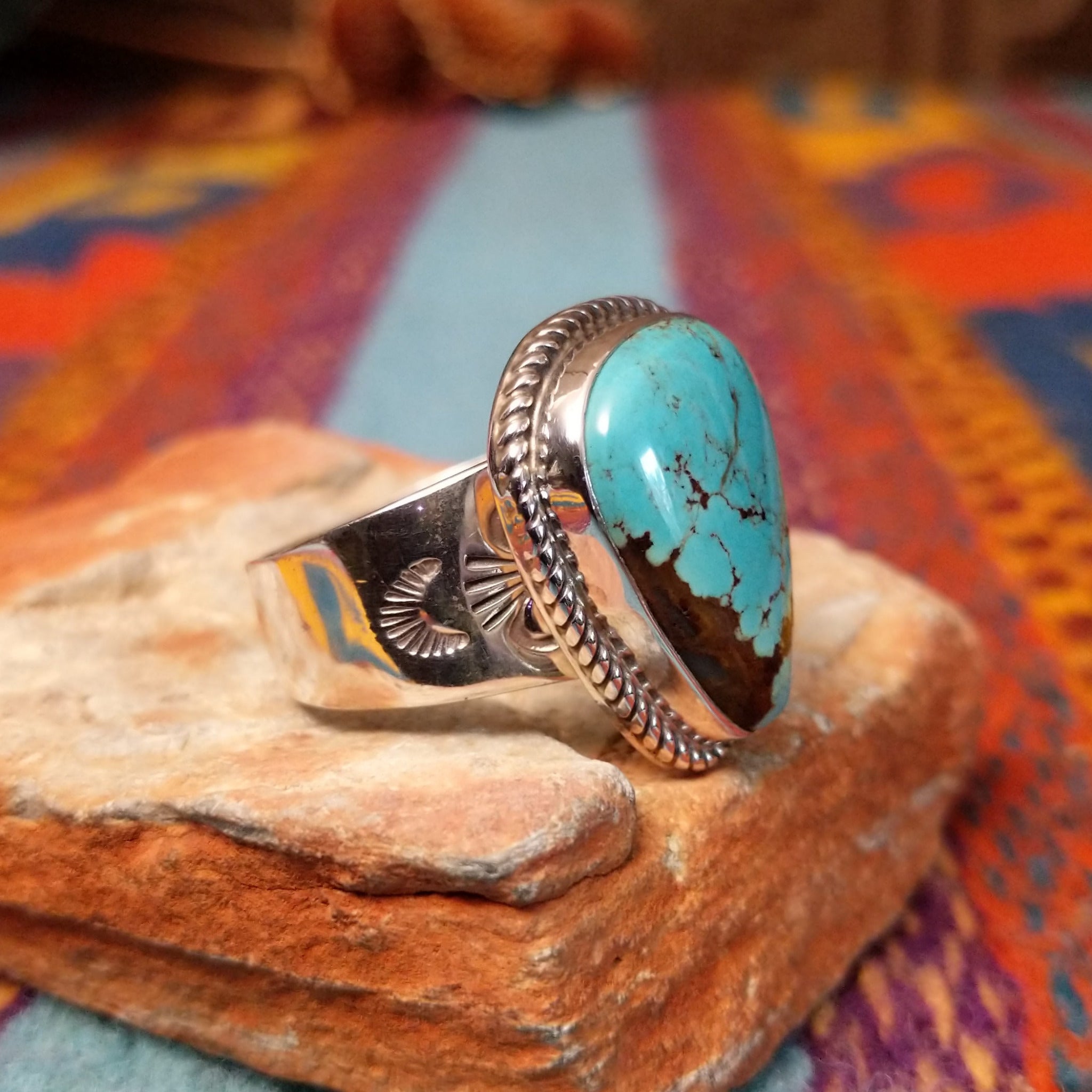 Navajo #8 Turquoise Ring featuring a large freeform blue turquoise cabochon with prominent brown matrix, framed by twisted silver rope detailing in a polished silver setting; side view.
