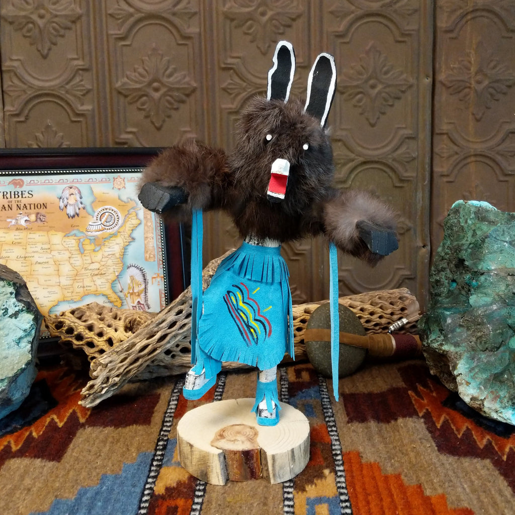 Wood carved into a bear kachina with fur body, blue suede clothing, and paint.