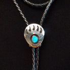 A sterling silver bolo tie necklace featuring a paw print design with a turquoise stone inlay, displayed on a black background.