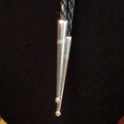 A silver bolo tie necklace with a braided black cord, a turquoise stone, and a polished metal drop, displayed on a black mannequin bust.