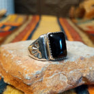Navajo Black Onyx Ring featuring a polished rectangular black onyx gemstone in a sawtooth silver bezel, with a wide silver band accented by stamped fan-shaped designs on both sides; side view.