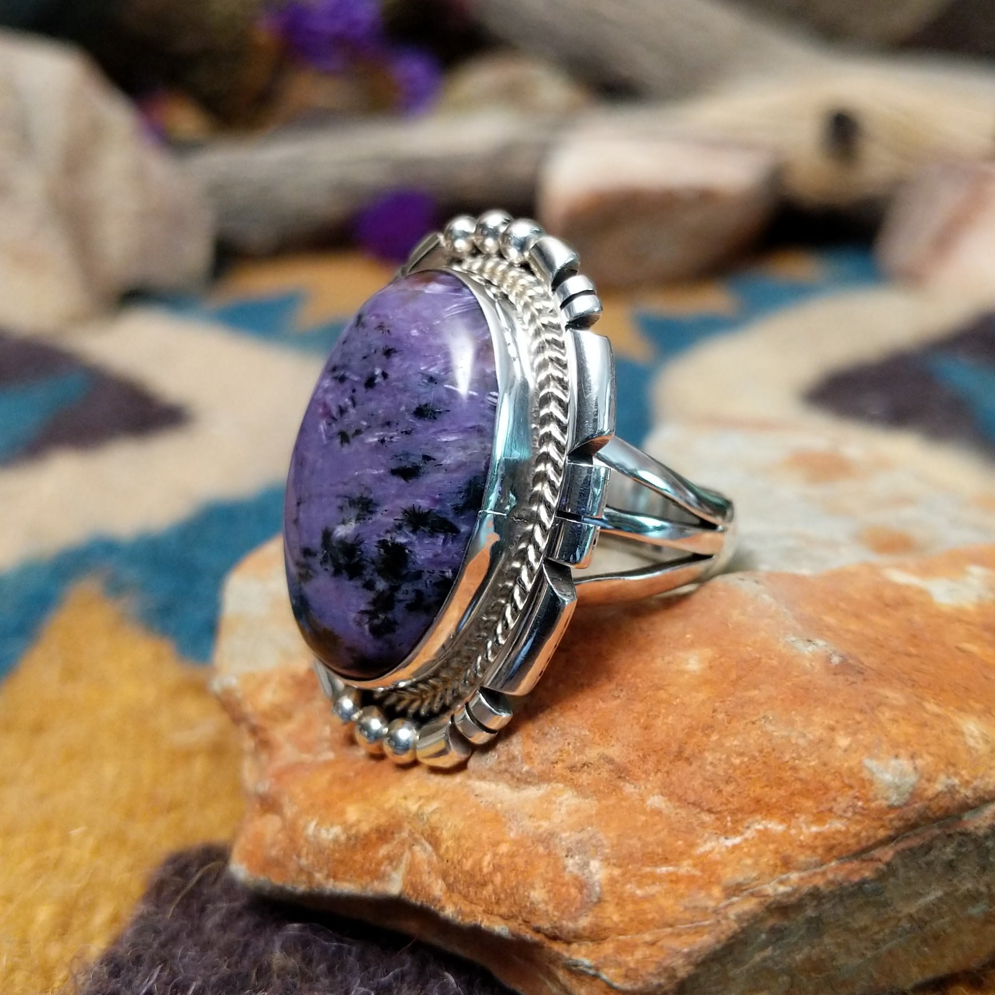 Navajo sterling silver ring with an oval Charoite stone in shades of purple with natural black inclusions; side view.