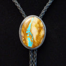 A Sterling Silver bolo tie necklace featuring an oval Boulder Turquoise pendant, suspended on a braided cord against a black background.