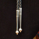A close-up of the bolo tie silver tips, set against a black textured background.