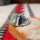 Navajo Boulder Turquoise Ring by E. featuring a rectangular turquoise stone with prominent natural brown host rock, set in a polished silver band with geometric stamped accents; side view.