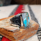 Navajo Boulder Turquoise Ring by E. featuring a rectangular turquoise stone with prominent natural brown host rock, set in a polished silver band with geometric stamped accents; side view.