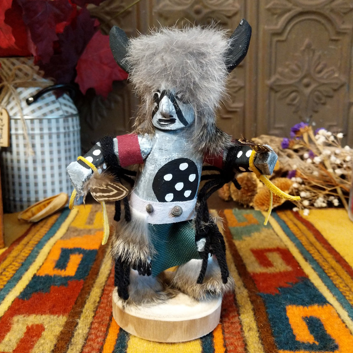 This distinctive Navajo Buffalo Kachina by Debbie James features a hand-painted wooden figure with black buffalo horns, gray fur headdress, black-and-white painted details, natural feathers, leather ties, and a wooden display base.