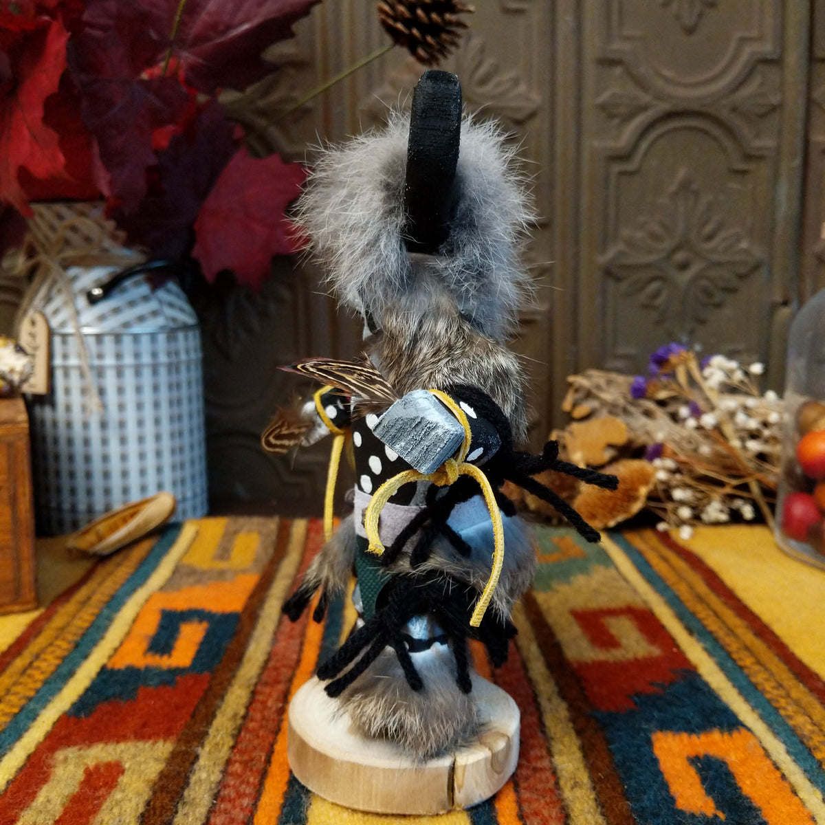 This distinctive Navajo Buffalo Kachina by Debbie James features a hand-painted wooden figure with black buffalo horns, gray fur headdress, black-and-white painted details, natural feathers, leather ties, and a wooden display base; side view.