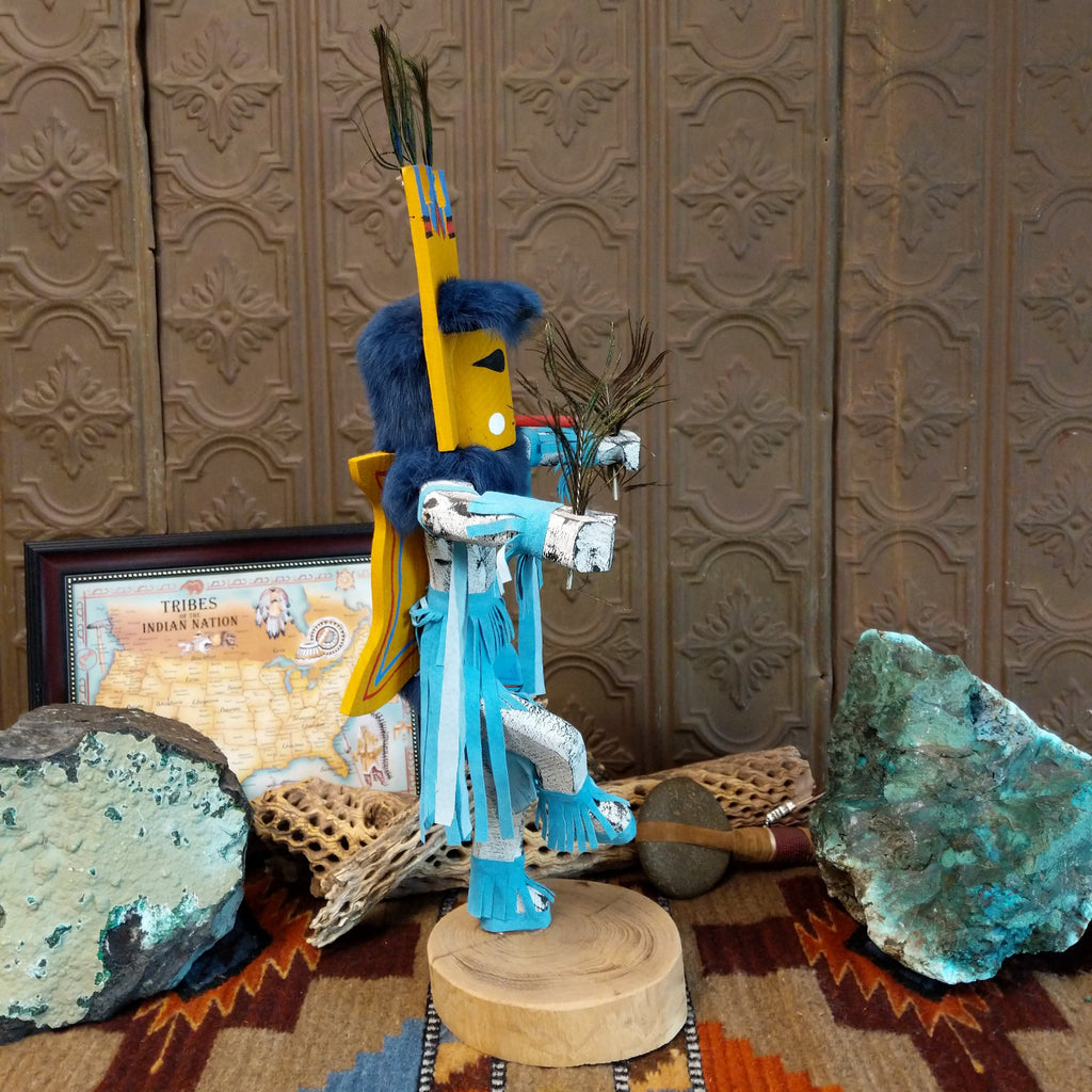 Wood carved into a butterfly kachina with vibrant paint, feathers, and blue suede.