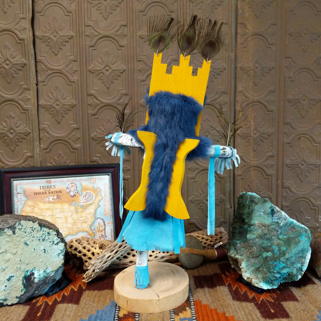Wood carved into a butterfly kachina with vibrant paint, feathers, and blue suede.