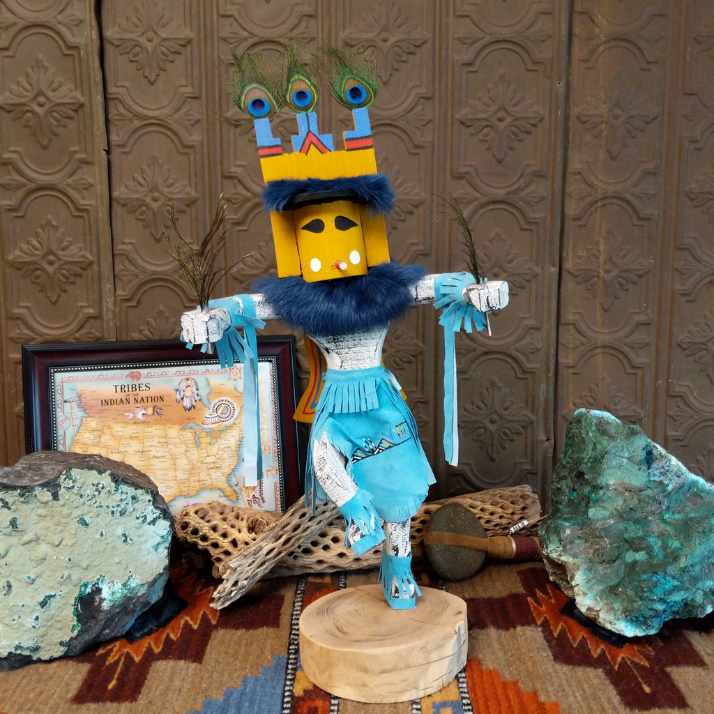 Wood carved into a butterfly kachina with vibrant paint, feathers, and blue suede.