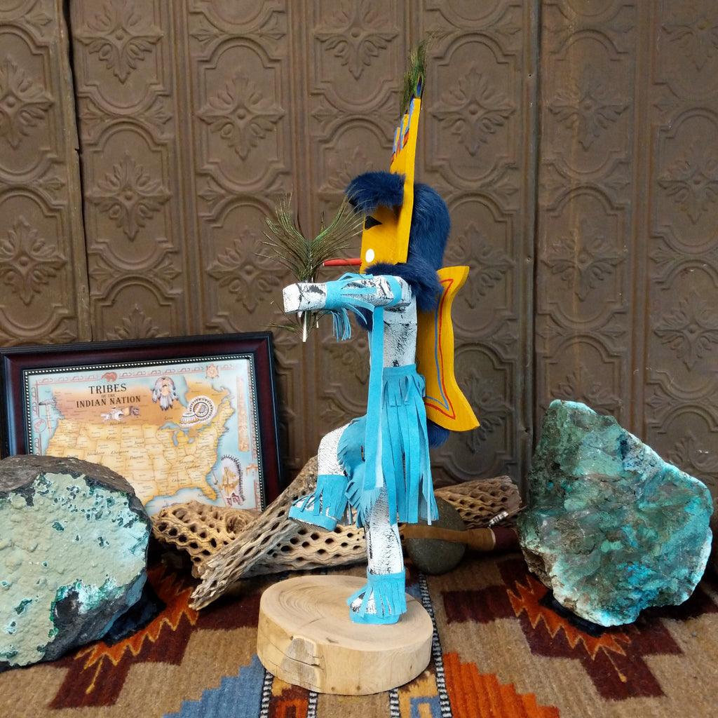Wood carved into a butterfly kachina with vibrant paint, feathers, and blue suede.
