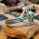 Handcrafted Navajo sterling silver cuff featuring an oval Carico Lake turquoise cabochon surrounded by ornate silver beadwork, scroll accents, and an open diamond-shaped frame; side view.