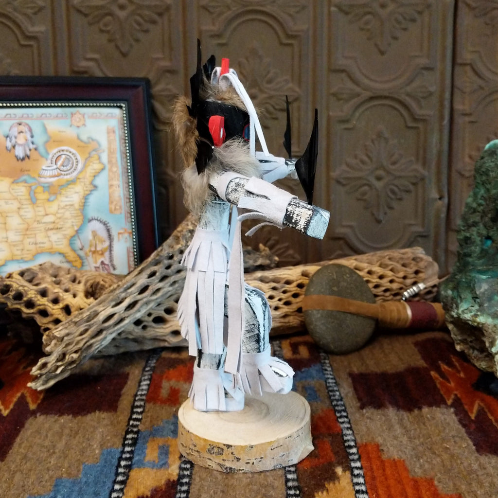 Wood carved into a chasing star kachina with white and vibrant paints, feathers, and fringe.