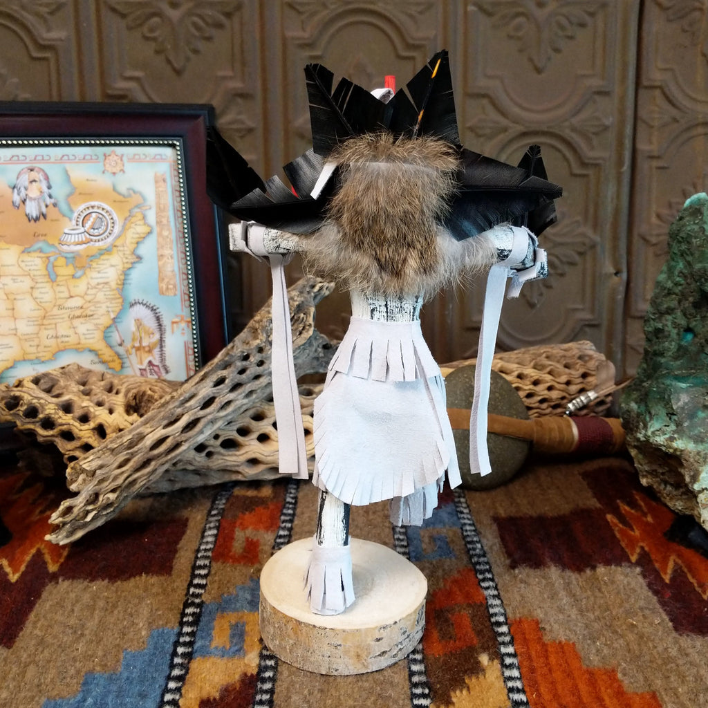 Wood carved into a chasing star kachina with white and vibrant paints, feathers, and fringe.