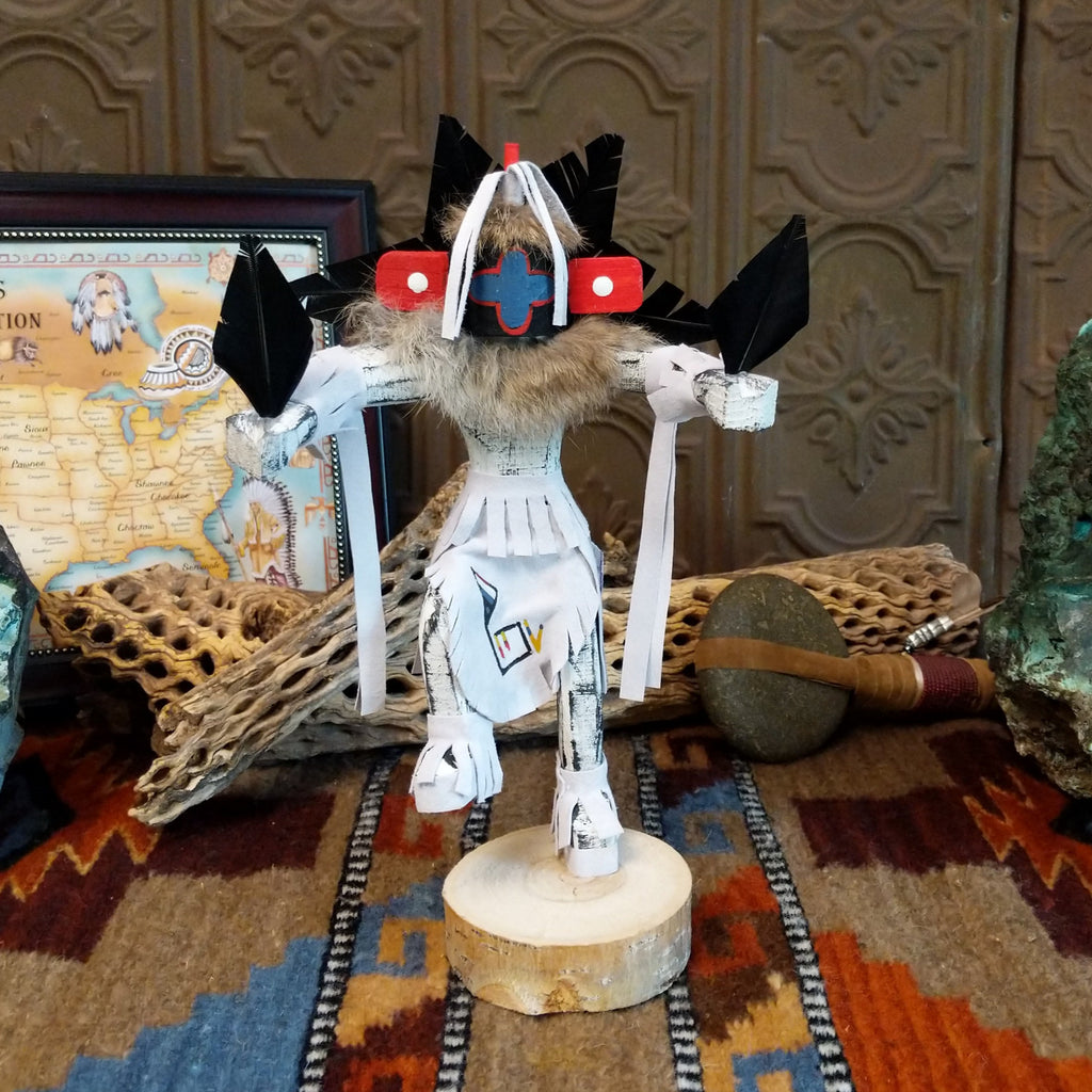 Wood carved into a chasing star kachina with white and vibrant paints, feathers, and fringe.