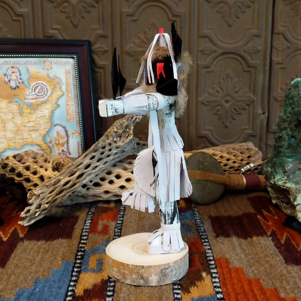 Wood carved into a chasing star kachina with white and vibrant paints, feathers, and fringe.