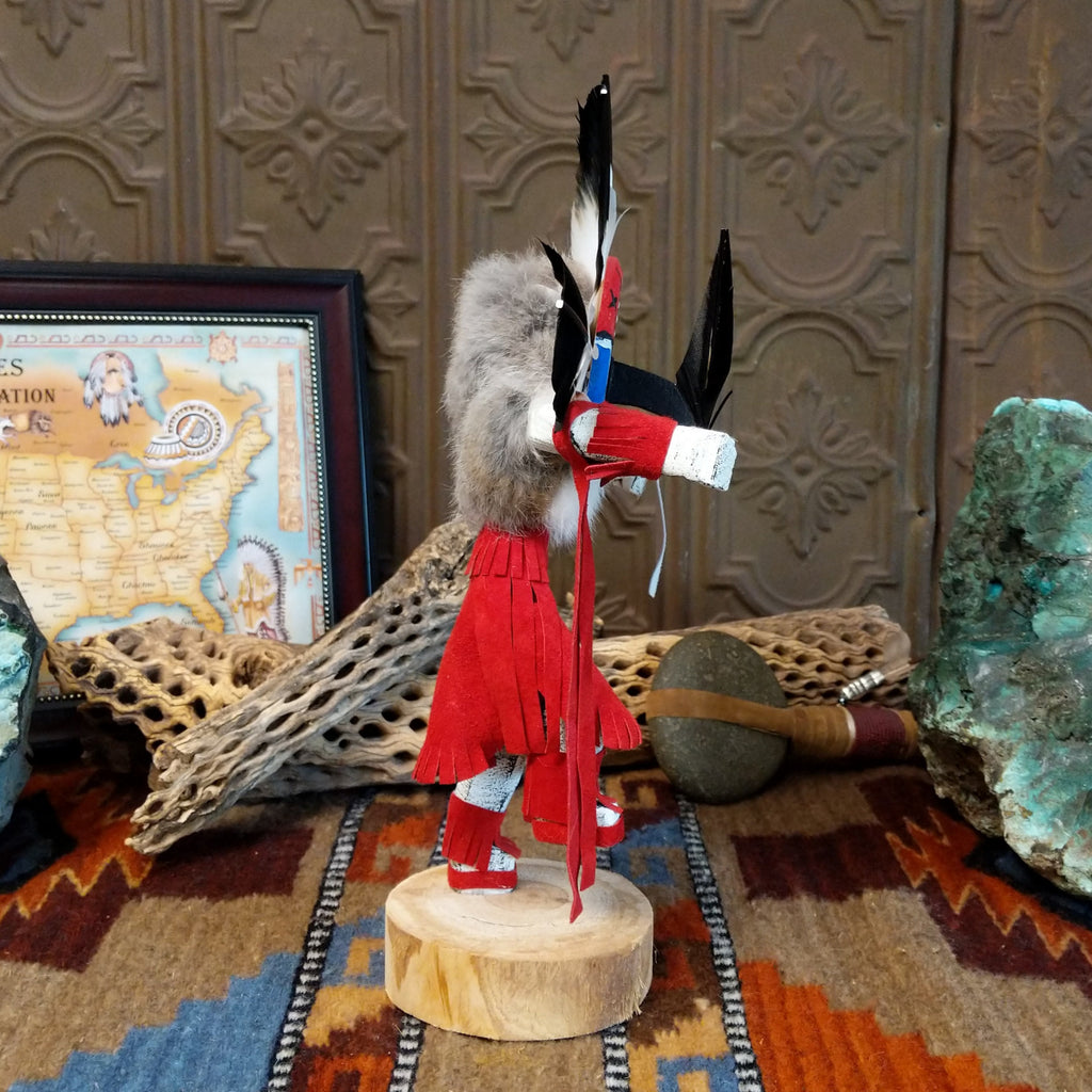 Wood carved into a chief kachina with feathers encircling its head, vibrant paint, and red suede clothing.