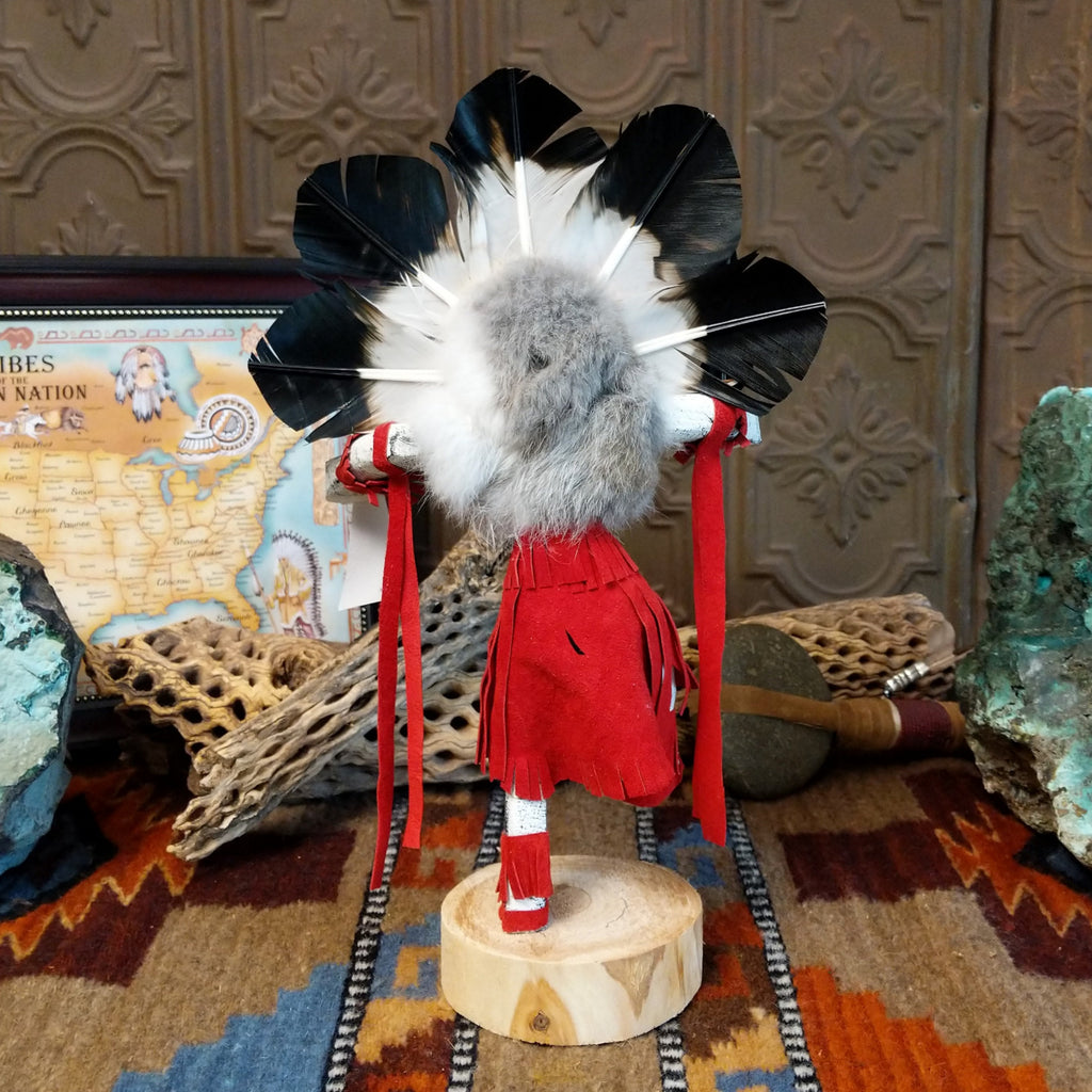 Wood carved into a chief kachina with feathers encircling its head, vibrant paint, and red suede clothing.