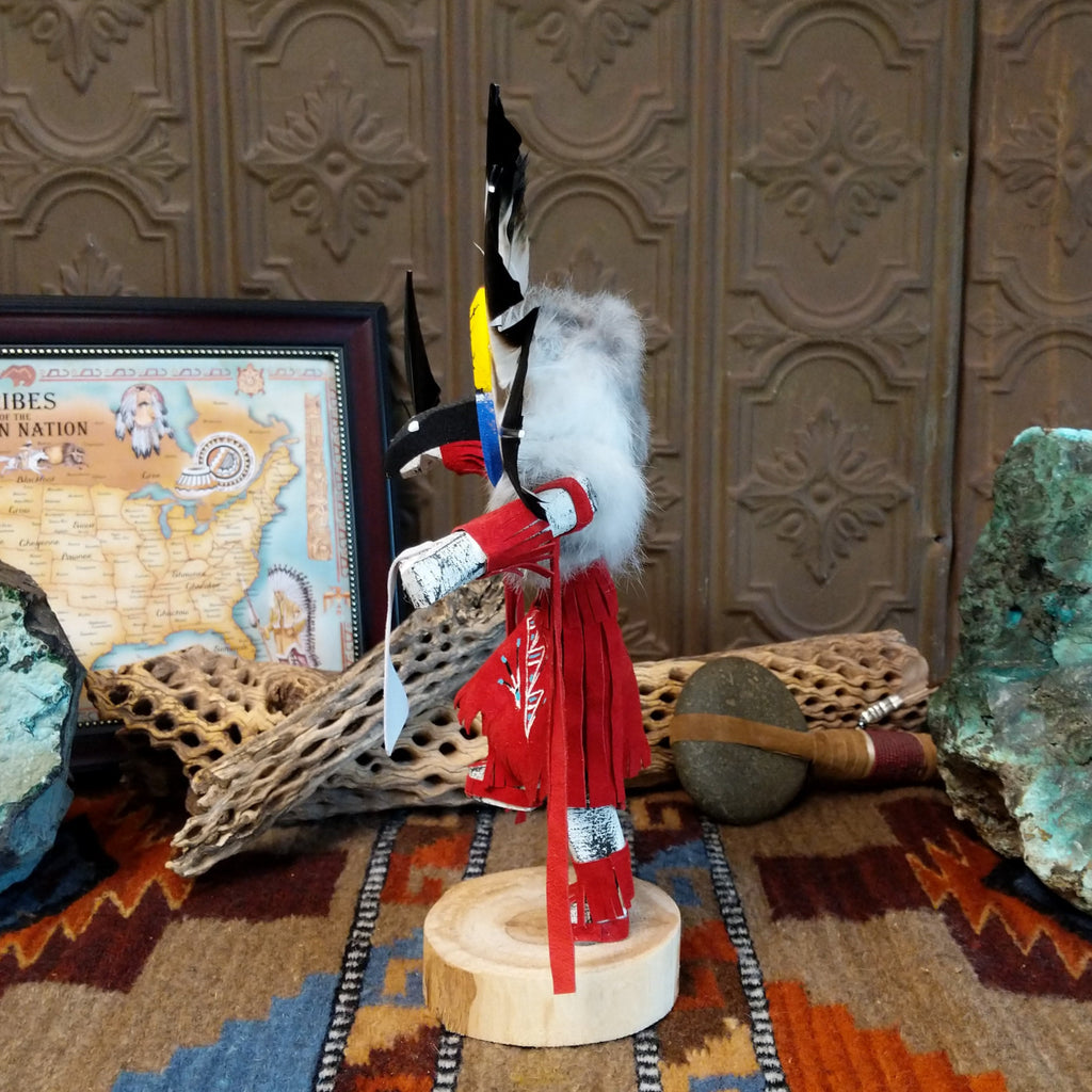 Wood carved into a chief kachina with feathers encircling its head, vibrant paint, and red suede clothing.