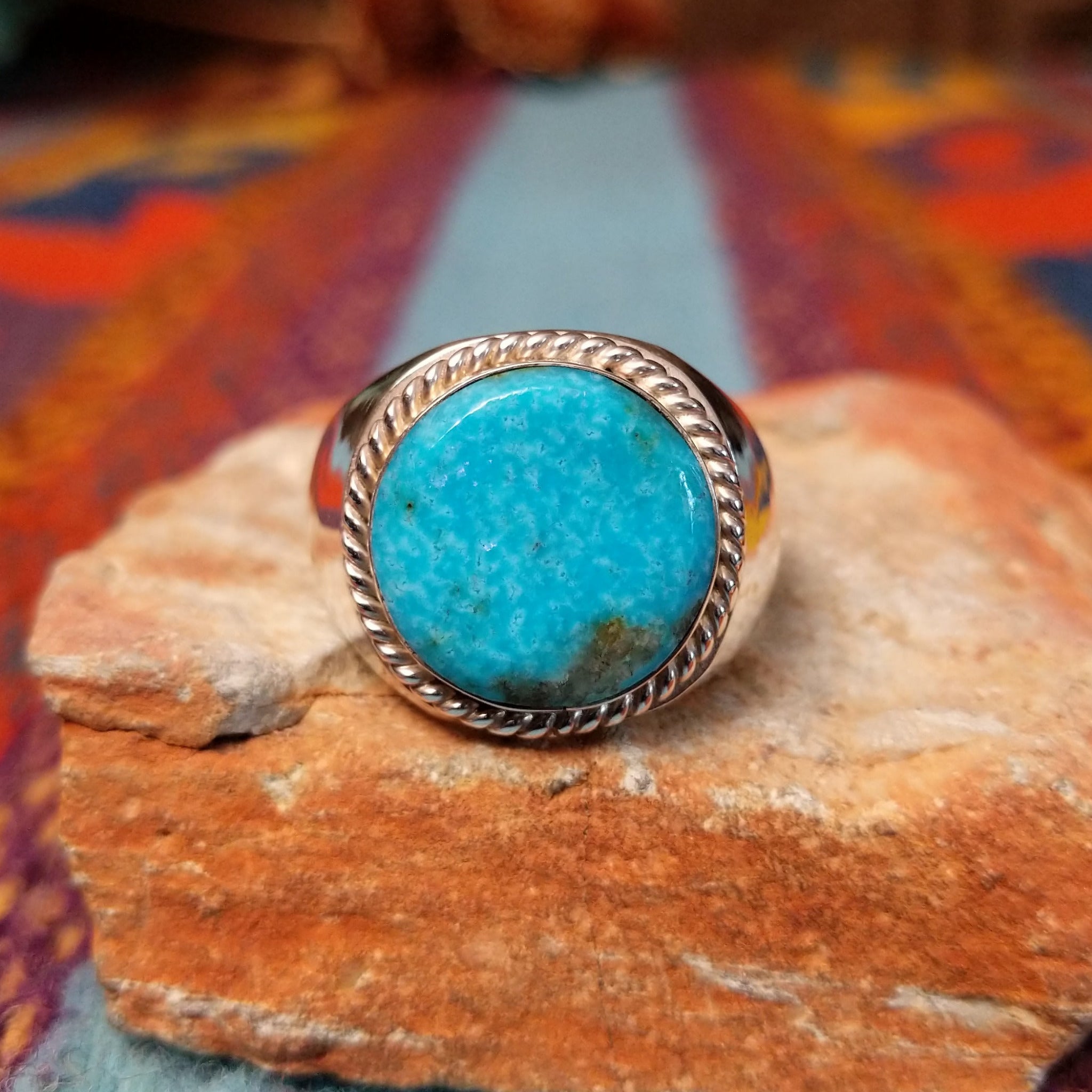 Navajo Circle Turquoise Ring by A.Q.J. featuring a large round blue turquoise cabochon with natural matrix, framed by twisted silver rope detailing on a polished silver band.