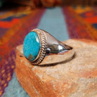 Navajo Circle Turquoise Ring by A.Q.J. featuring a large round blue turquoise cabochon with natural matrix, framed by twisted silver rope detailing on a polished silver band; side view.