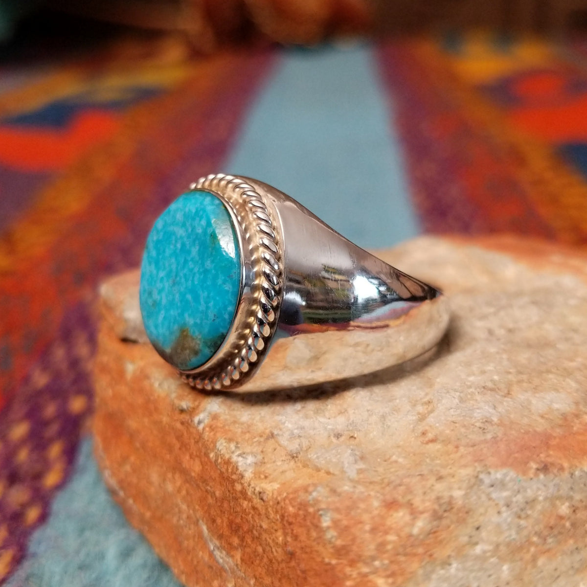 Navajo Circle Turquoise Ring by A.Q.J. featuring a large round blue turquoise cabochon with natural matrix, framed by twisted silver rope detailing on a polished silver band; side view.