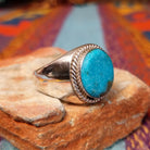 Navajo Circle Turquoise Ring by A.Q.J. featuring a large round blue turquoise cabochon with natural matrix, framed by twisted silver rope detailing on a polished silver band; side view.
