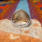 Navajo Circle Turquoise Ring by A.Q.J. featuring a large round blue turquoise cabochon with natural matrix, framed by twisted silver rope detailing on a polished silver band; underside view.
