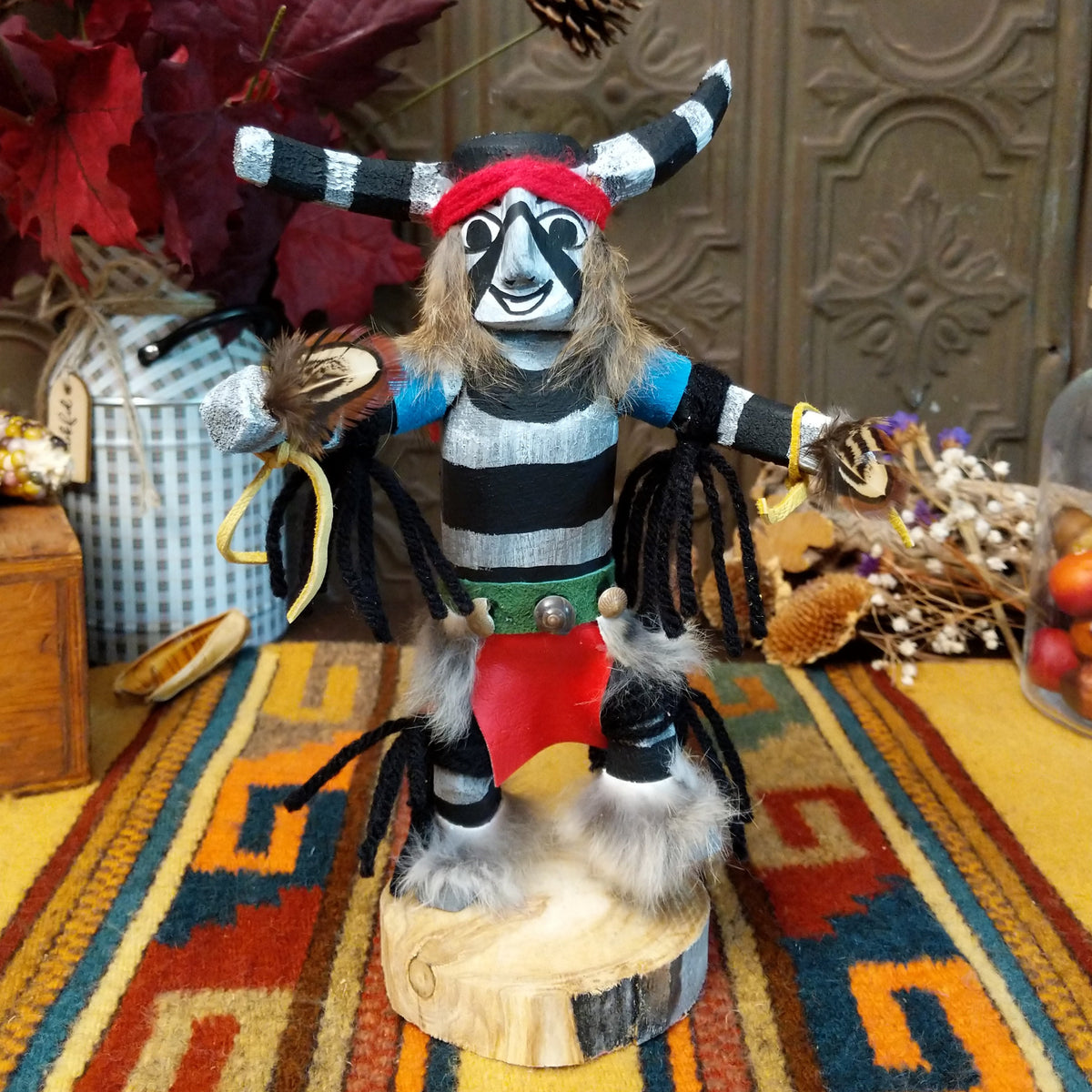 Navajo Clown Dancer Kachina doll with black-and-white striped body, curved horns, red headband, and feather accents.