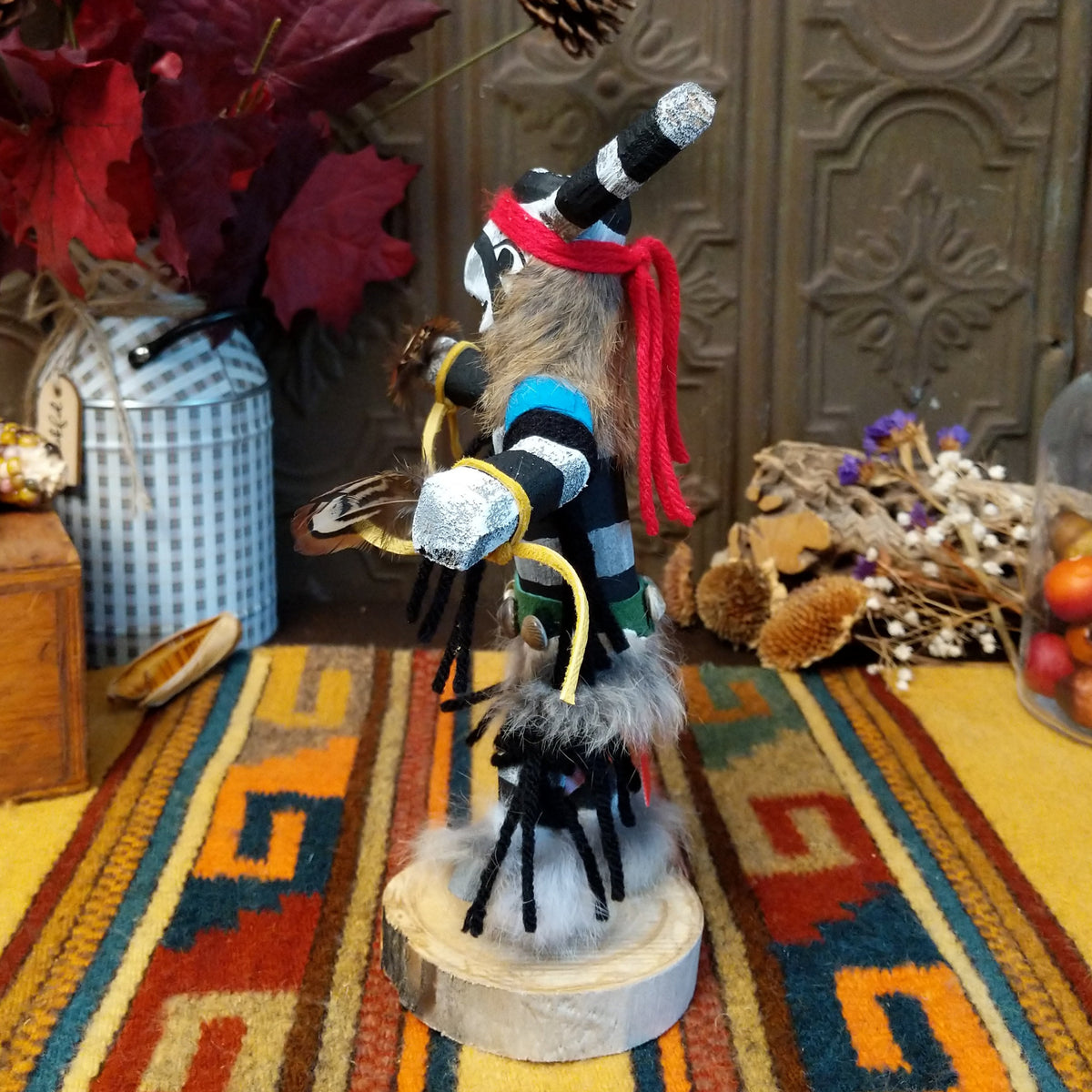 Side view of the Navajo Clown Dancer Kachina doll with black-and-white striped body, curved horns, red headband, and feather accents.