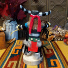 Back view of the Navajo Clown Dancer Kachina doll with black-and-white striped body, curved horns, red headband, and feather accents.