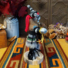 Side view of the Navajo Clown Dancer Kachina doll with black-and-white striped body, curved horns, red headband, and feather accents.