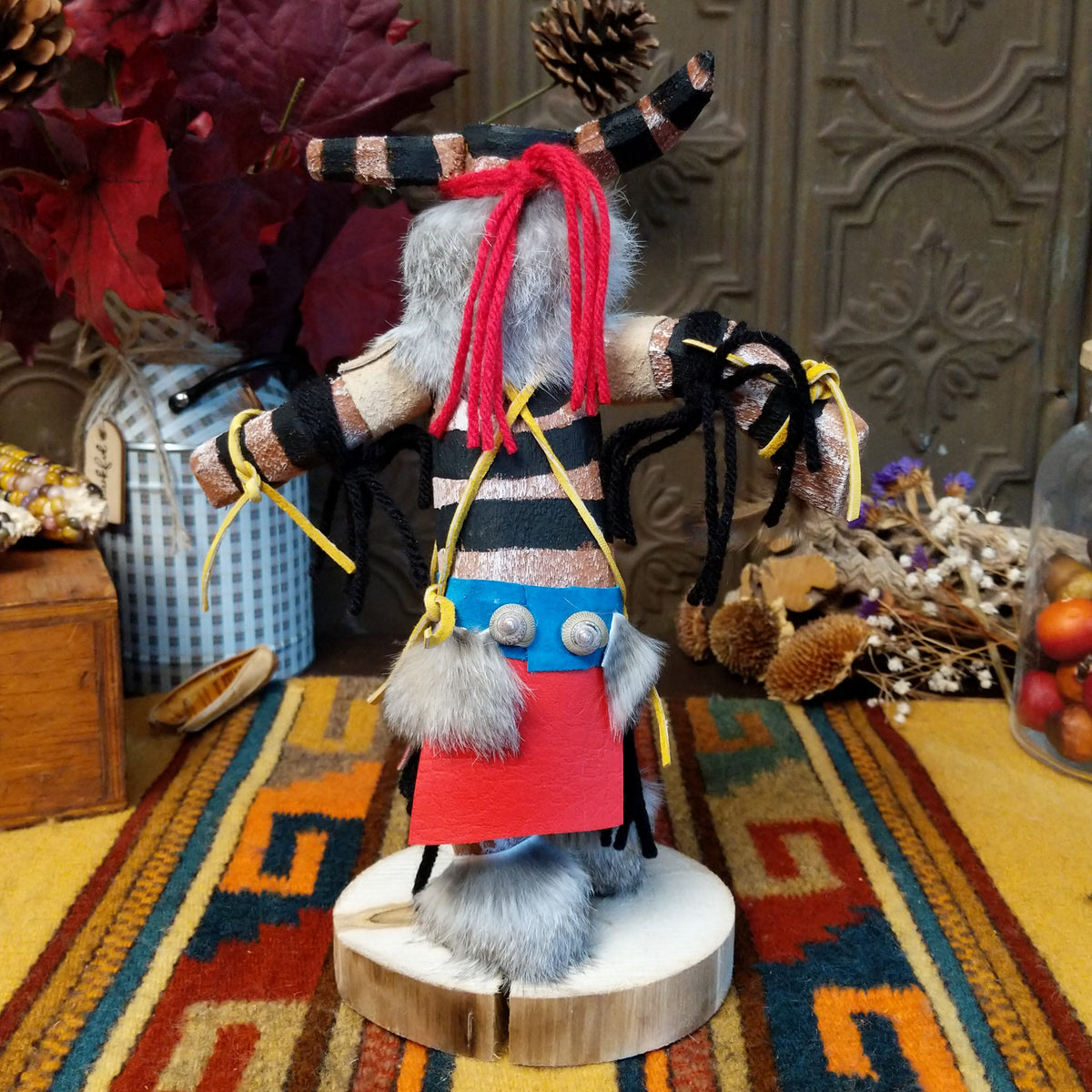 Back view of the Navajo Ogre Kachina doll with gray fur-covered face, black horns with turquoise markings, open red mouth, pointed teeth, and green fabric apron.