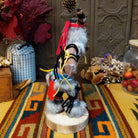Side view of the Navajo Ogre Kachina doll with gray fur-covered face, black horns with turquoise markings, open red mouth, pointed teeth, and green fabric apron.
