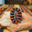 Front view of a sterling silver coral cluster ring featuring an elongated center stone surrounded by teardrop-shaped red-orange coral stones, twisted rope detailing, and oxidized silver accents.