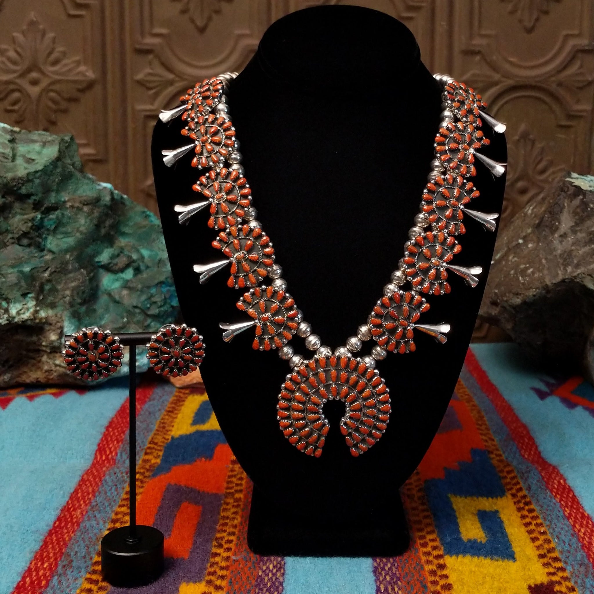 Navajo sterling silver squash blossom necklace and matching earrings by B.Y., featuring numerous red-orange coral stones arranged in floral clusters and a large coral-covered Naja pendant.