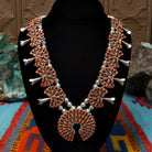 Navajo sterling silver squash blossom necklace and matching earrings by B.Y., featuring numerous red-orange coral stones arranged in floral clusters and a large coral-covered Naja pendant.