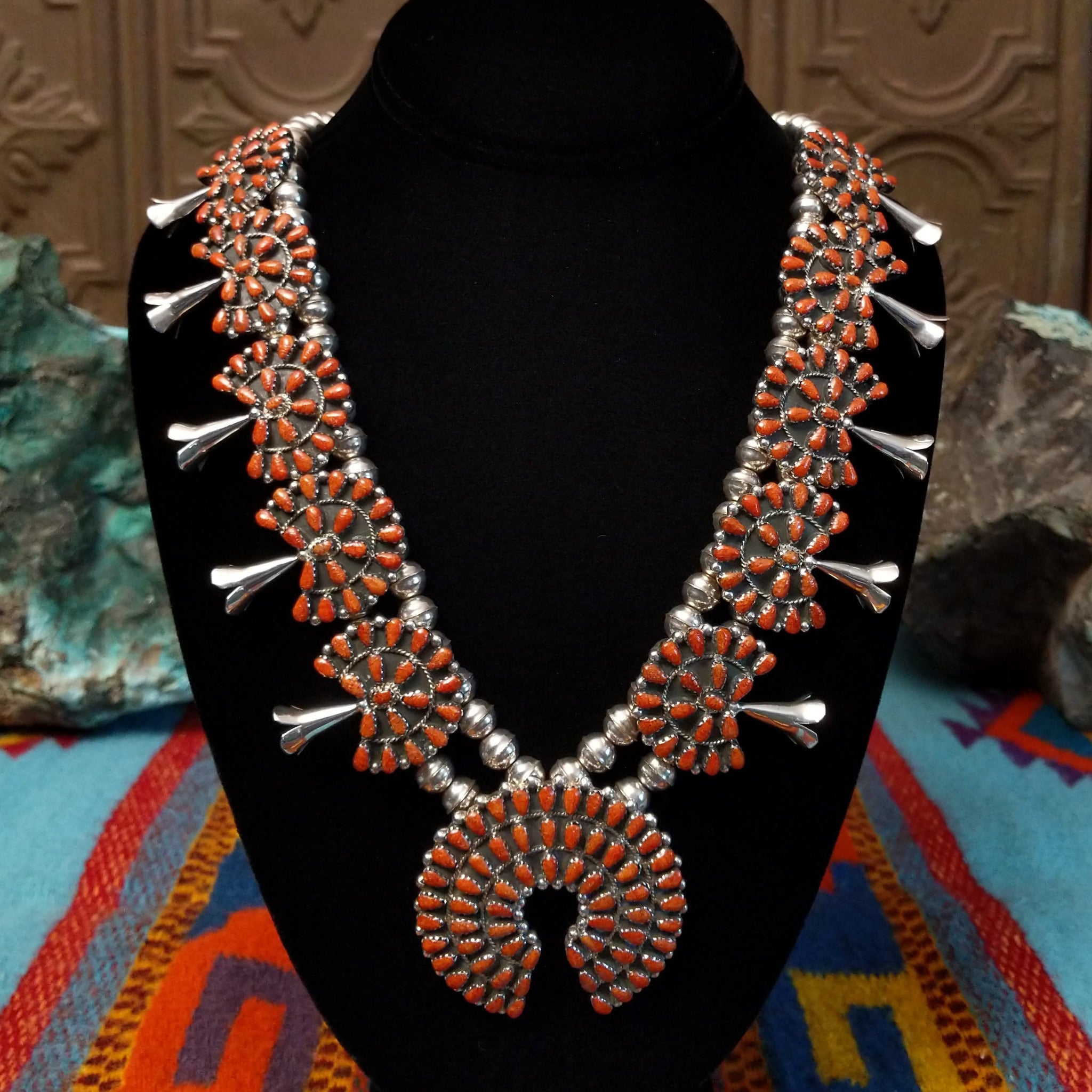 Navajo sterling silver squash blossom necklace and matching earrings by B.Y., featuring numerous red-orange coral stones arranged in floral clusters and a large coral-covered Naja pendant.