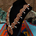 Navajo sterling silver squash blossom necklace and matching earrings by B.Y., featuring numerous red-orange coral stones arranged in floral clusters and a large coral-covered Naja pendant; side view.