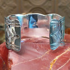 Sterling silver cuff with coral set in a septet of bezels, framed by ornate stamping and silverwork.