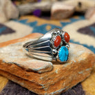 Handcrafted Navajo sterling silver ring featuring two natural red coral cabochons and one blue turquoise cabochon with traditional sawtooth bezels, silver raindrop accents, and a split-shank band; side view.