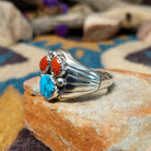 Handcrafted Navajo sterling silver ring featuring two natural red coral cabochons and one blue turquoise cabochon with traditional sawtooth bezels, silver raindrop accents, and a split-shank band; side view.