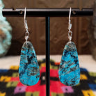 Navajo Dark Matrix Slab Turquoise Earrings featuring elongated blue turquoise stones with bold black and gray matrix patterns, suspended from silver hooks; backside view.