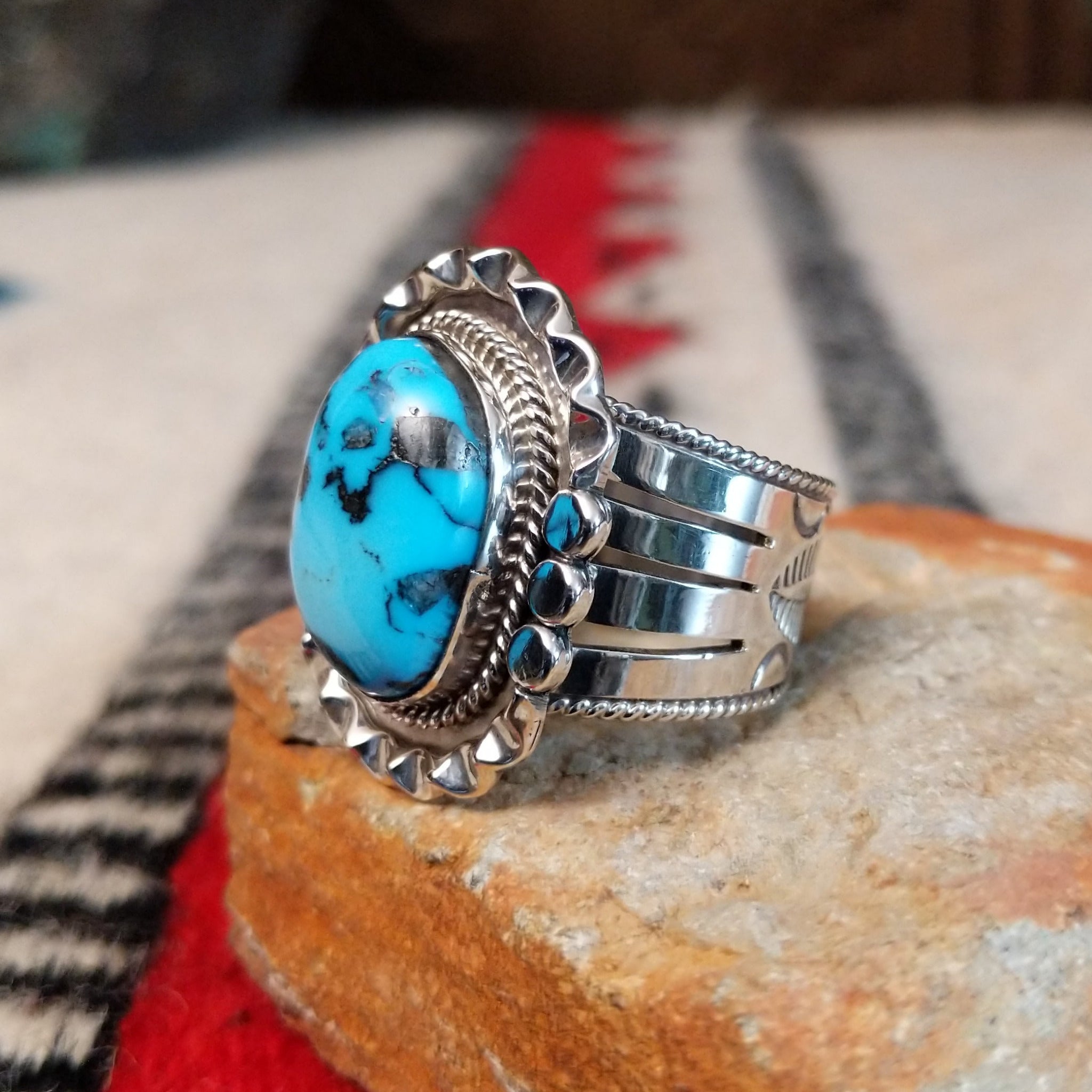 Navajo turquoise ring featuring a large oval bright blue turquoise stone with dark matrix, framed by twisted silver rope and an ornate scalloped silver setting; side view.