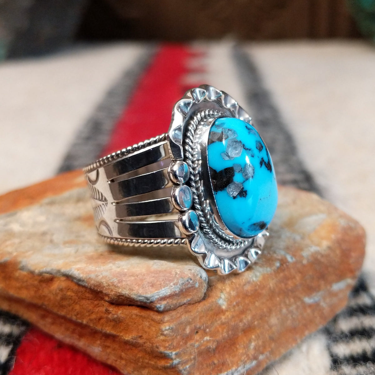 Navajo turquoise ring featuring a large oval bright blue turquoise stone with dark matrix, framed by twisted silver rope and an ornate scalloped silver setting; side view.