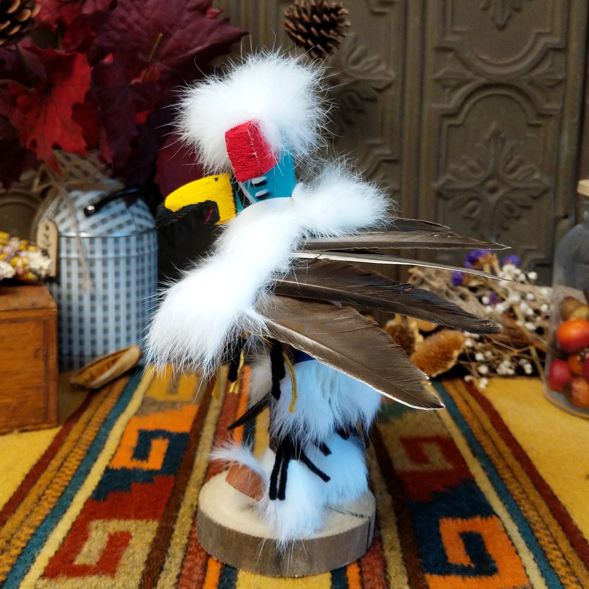 This striking Navajo Eagle Dancer Kachina by Debbie James features a colorful hand-painted eagle mask, white feather wings, fluffy headdress, leather ties, decorative clothing, and a wooden display base; side view.