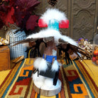 This striking Navajo Eagle Dancer Kachina by Debbie James features a colorful hand-painted eagle mask, white feather wings, fluffy headdress, leather ties, decorative clothing, and a wooden display base; back view.