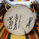 This striking Navajo Eagle Dancer Kachina by Debbie James features a colorful hand-painted eagle mask, white feather wings, fluffy headdress, leather ties, decorative clothing, and a wooden display base; artisan and product name on bottom.