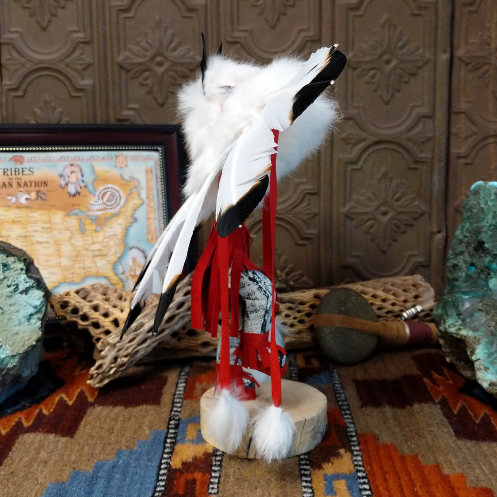 Wood carved into an eagle kachina with vibrant paints, feathers, and red suede clothing.